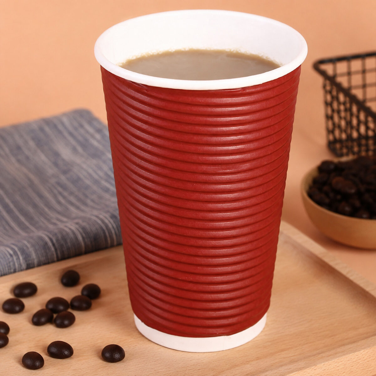 Red horizontally ribbed paper cup filled with coffee on a wooden tray beside beans