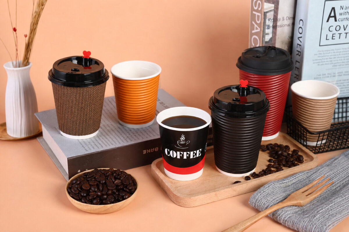 Six textured and printed coffee cups with lids, heart stoppers and coffee beans on a peach tabletop