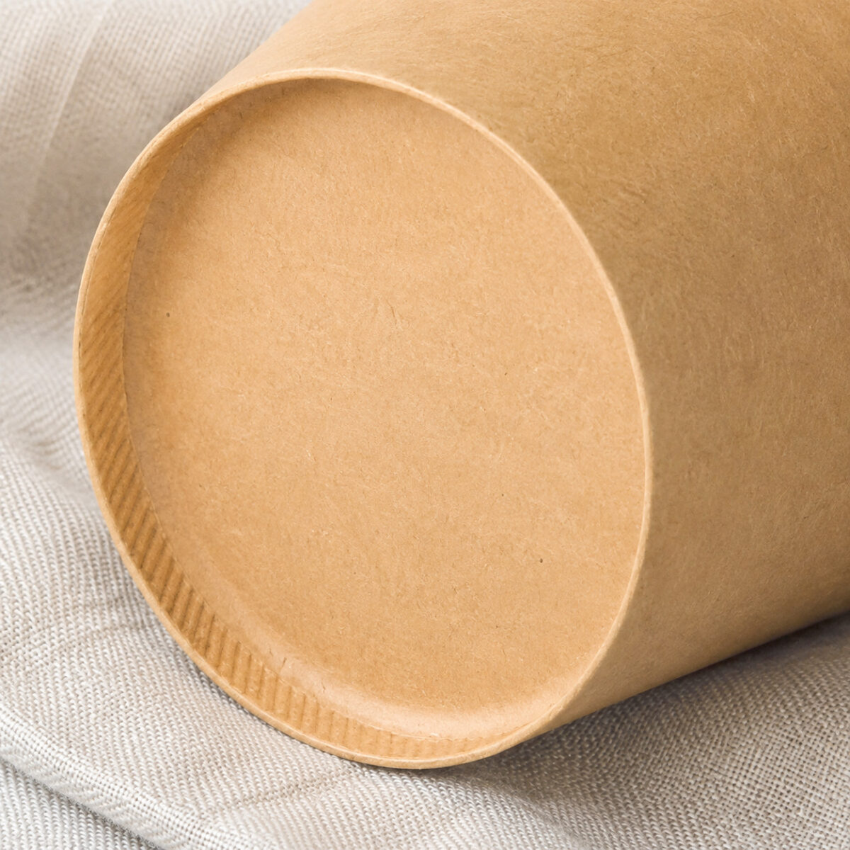 Shallow recessed kraft paper food-container base with a crimped foot ring on gray linen