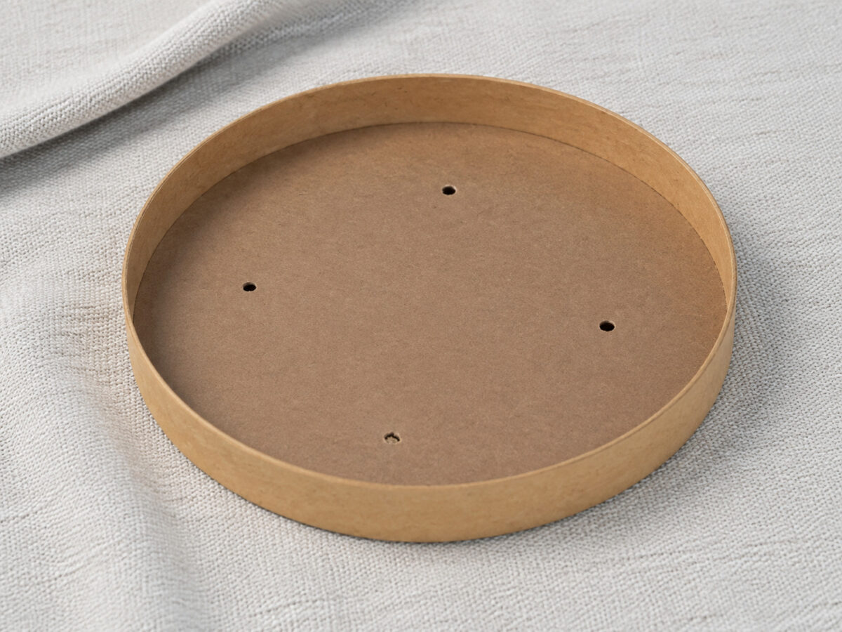 Inside of a kraft paper lid with four small ventilation holes on gray woven linen