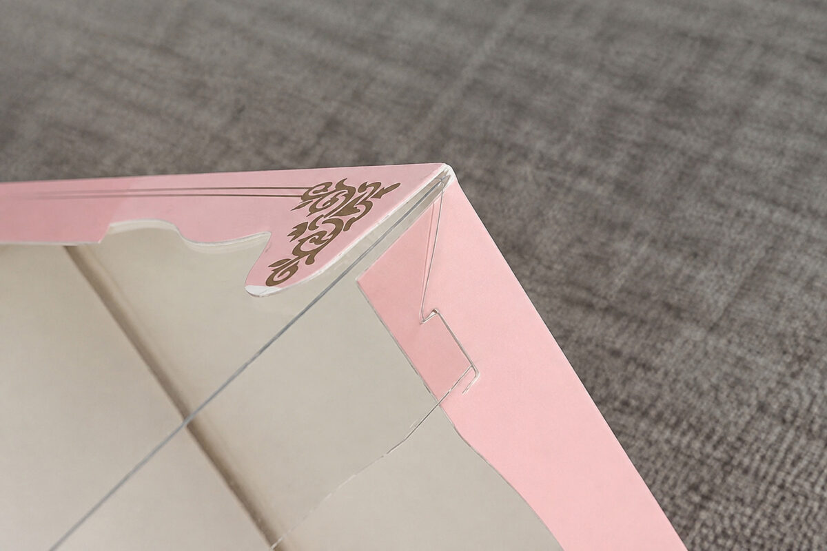 Clear folding side-wall tab beside the pink printed corner of a cake box