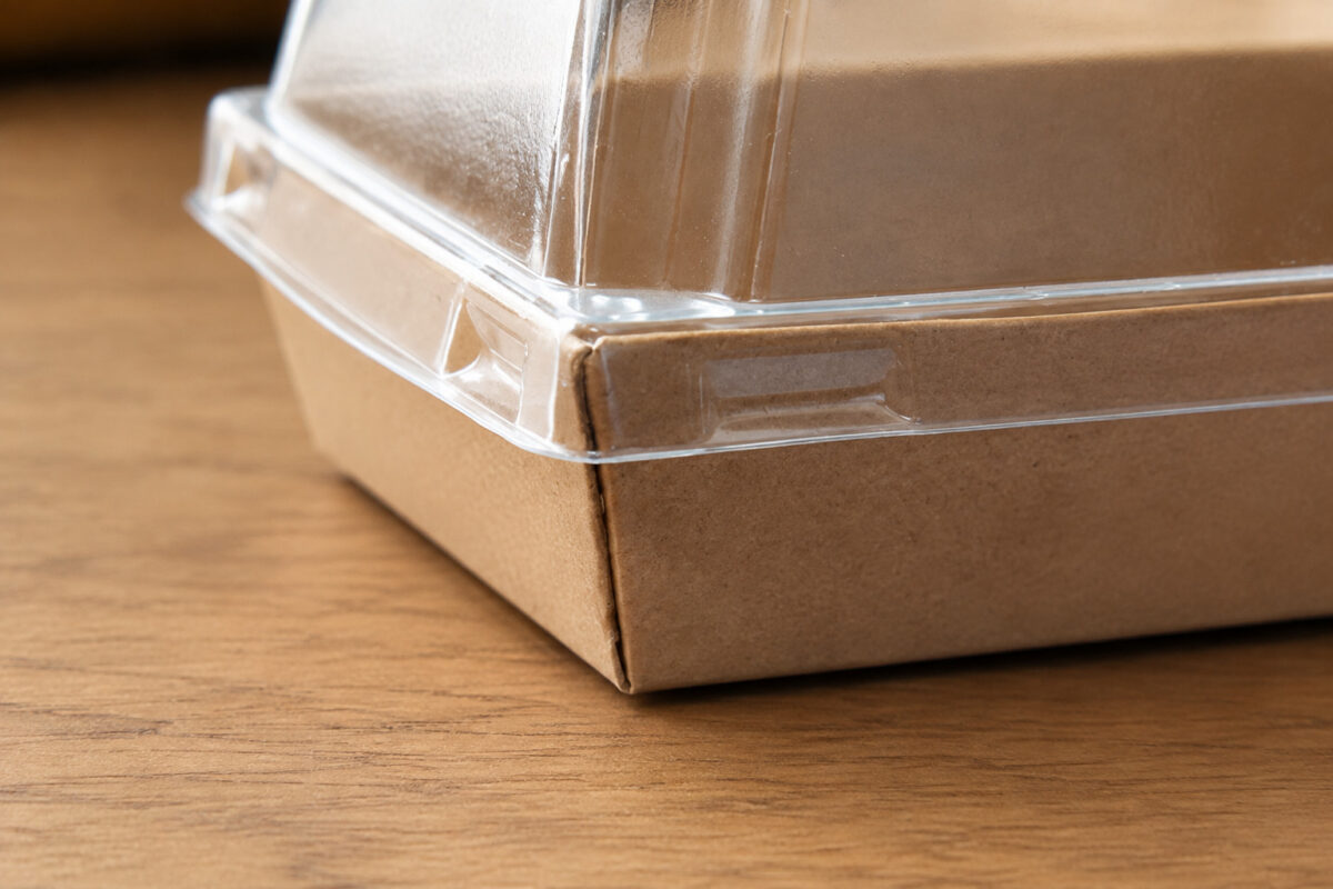 Close-up of a clear molded lid flange fitting a folded kraft dessert tray