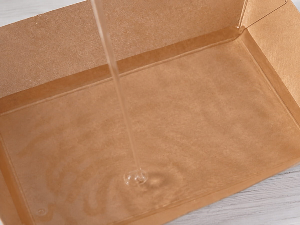 Clear liquid being poured into the inside of a kraft paper dessert tray