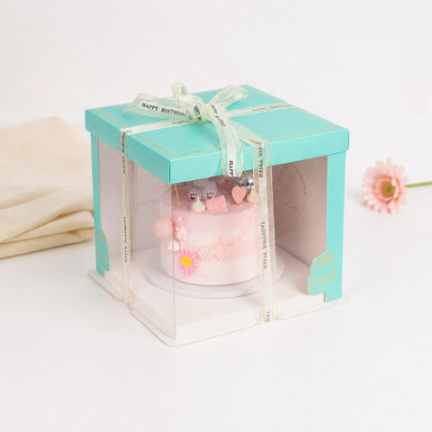 Turquoise clear-panel cake box with a pink birthday cake and cream Happy Birthday ribbon