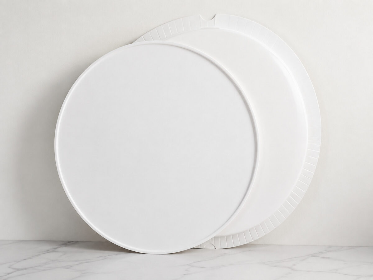 White round cake box lid and folded-edge circular base leaning against a wall