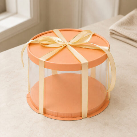 Colored Round Clear Cake Boxes Clear round cake box with an orange lid and raised orange base tied with a gold-edged cream ribbon