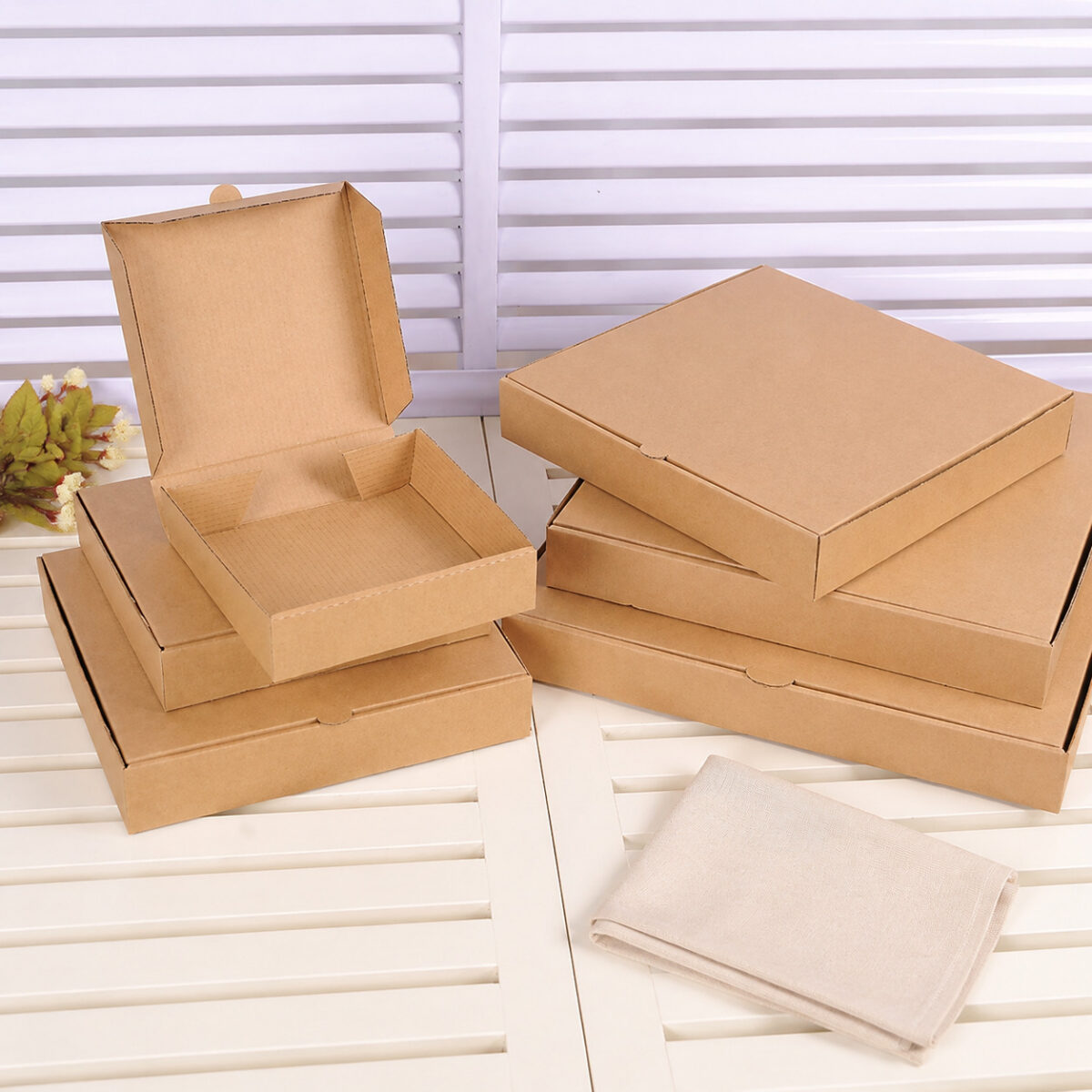 Six plain kraft pizza boxes including an open carton on a white slatted table