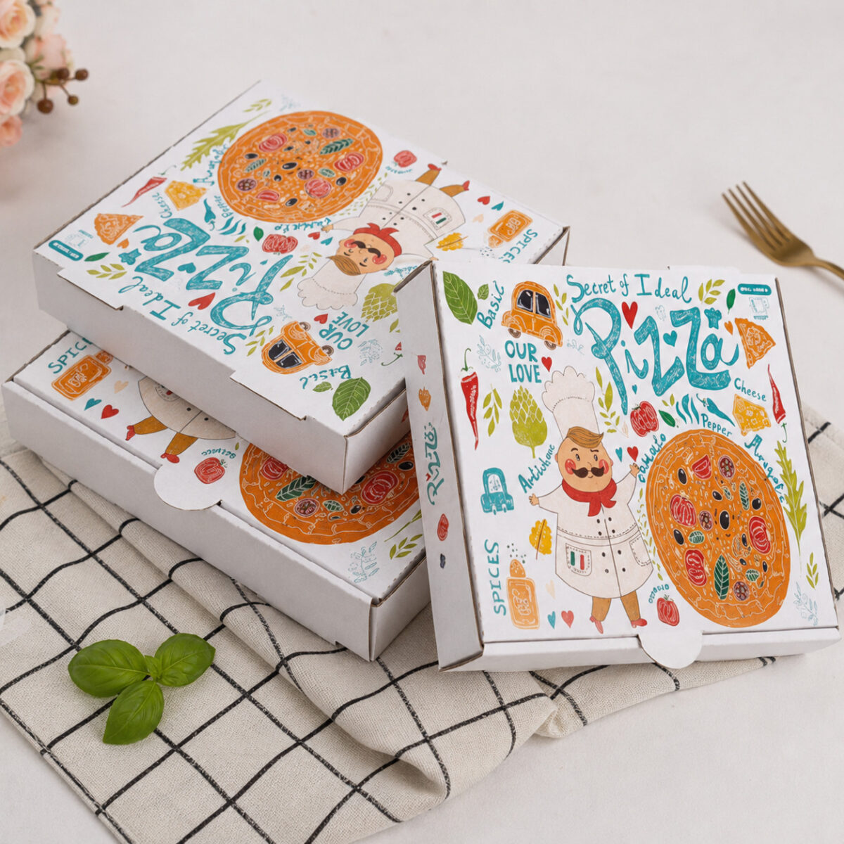 Three white pizza cartons with colorful chef illustrations on a checkered cloth