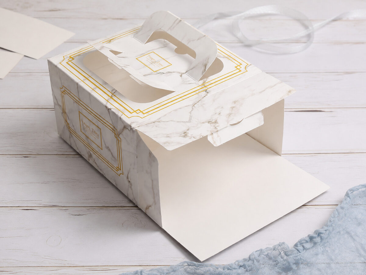 Open marble-print paper cake box with an integral handle and clear top window