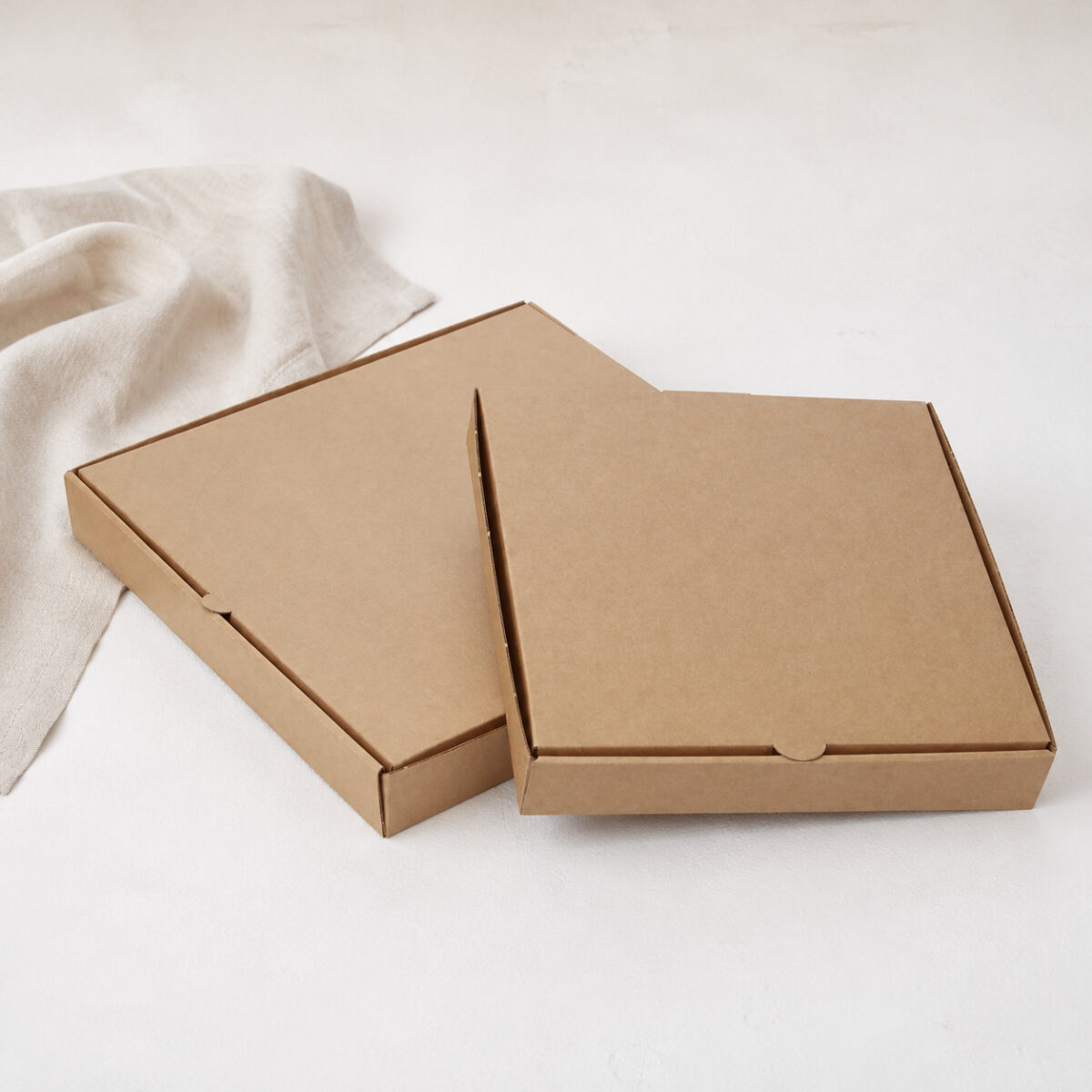 Two plain kraft pizza boxes with semicircular front tabs on a white table