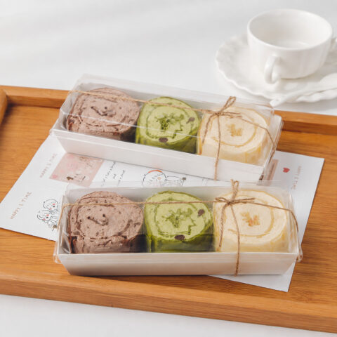 Two clear cake roll boxes with white trays, three assorted roll slices and natural twine