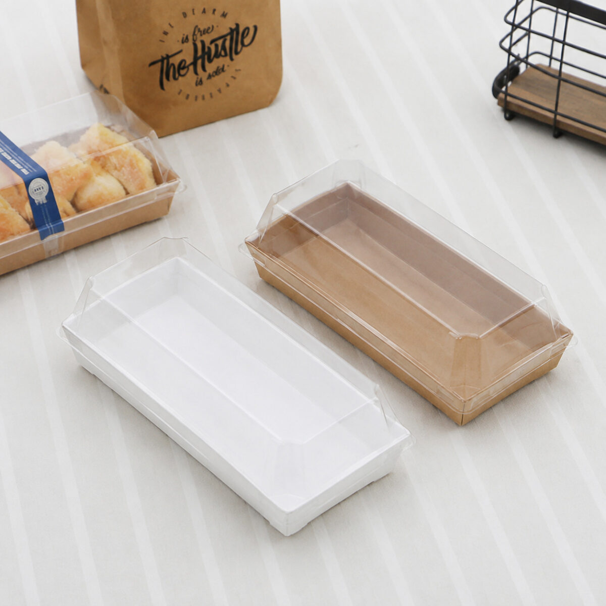 White and kraft rectangular paper dessert trays with clear fitted lids on a light tablecloth