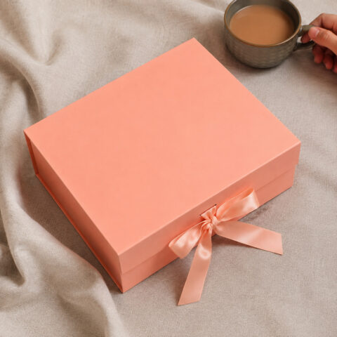 Peach presentation box with a matching satin bow beside a coffee cup on beige linen