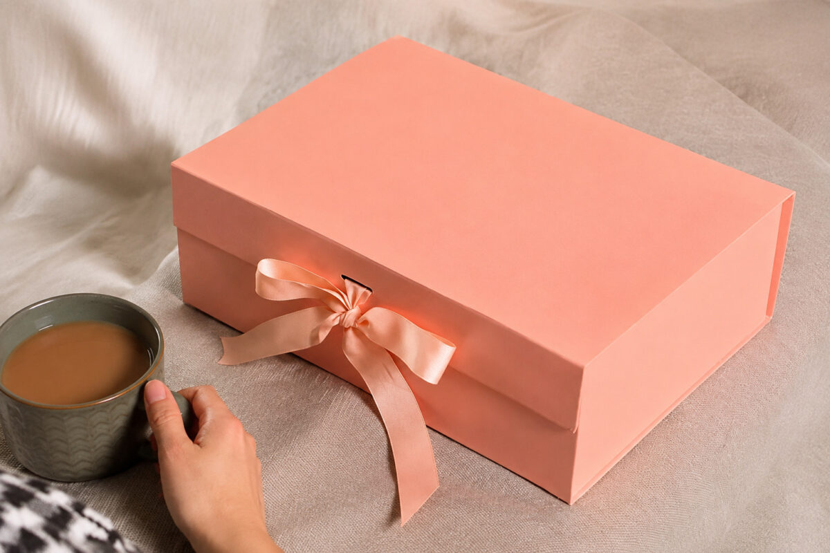 Peach ribbon gift box on a fabric-covered table beside a hand holding a mug