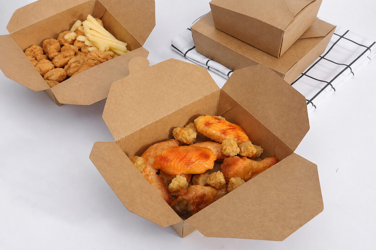 Open kraft takeaway cartons with chicken and fries beside two stacked closed boxes