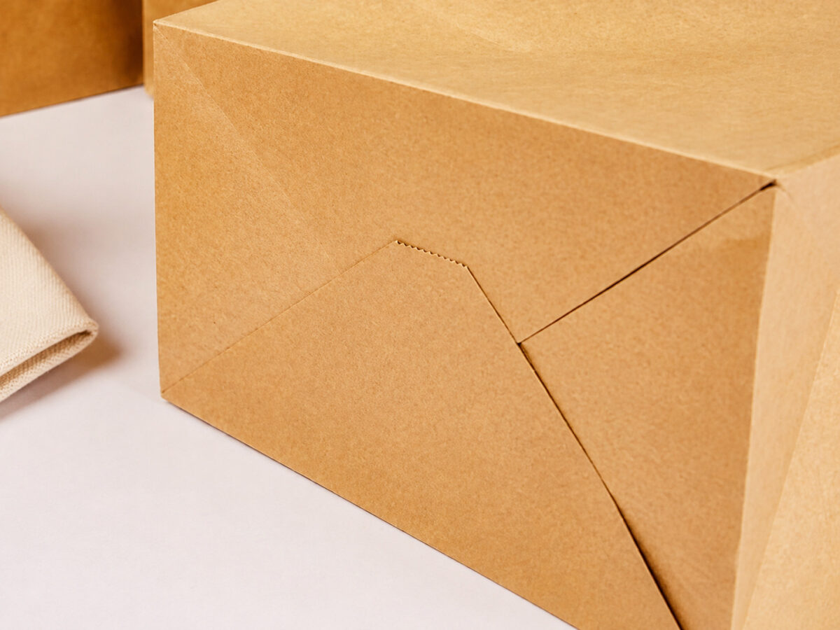 Close-up of overlapping folded flaps and the glued bottom corner of a kraft takeaway bag