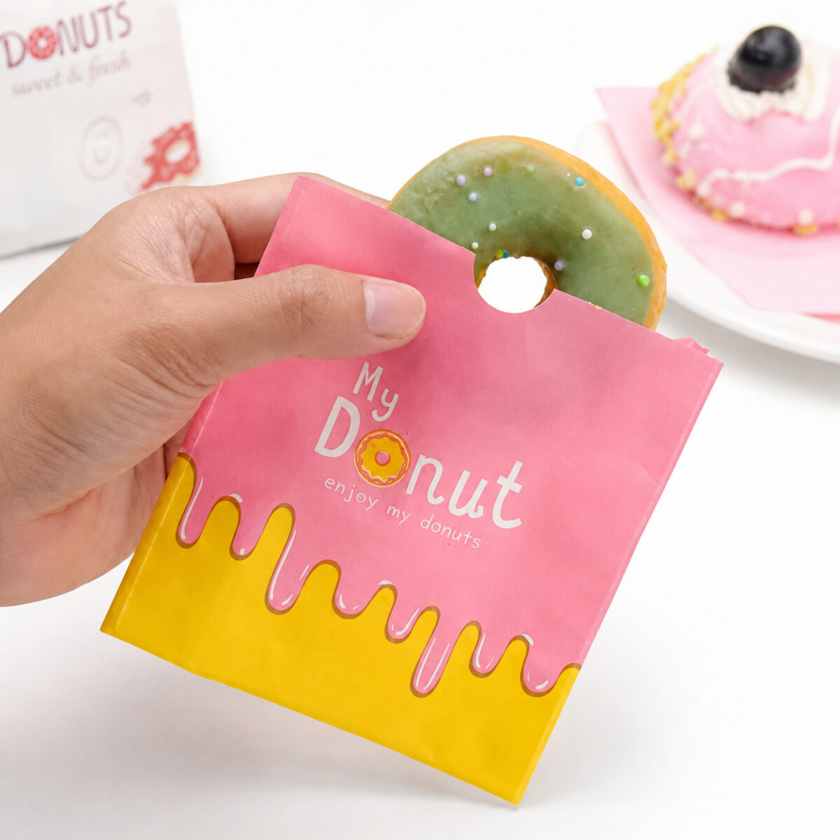 Pink My Donut paper sleeve holding a green iced donut in a hand