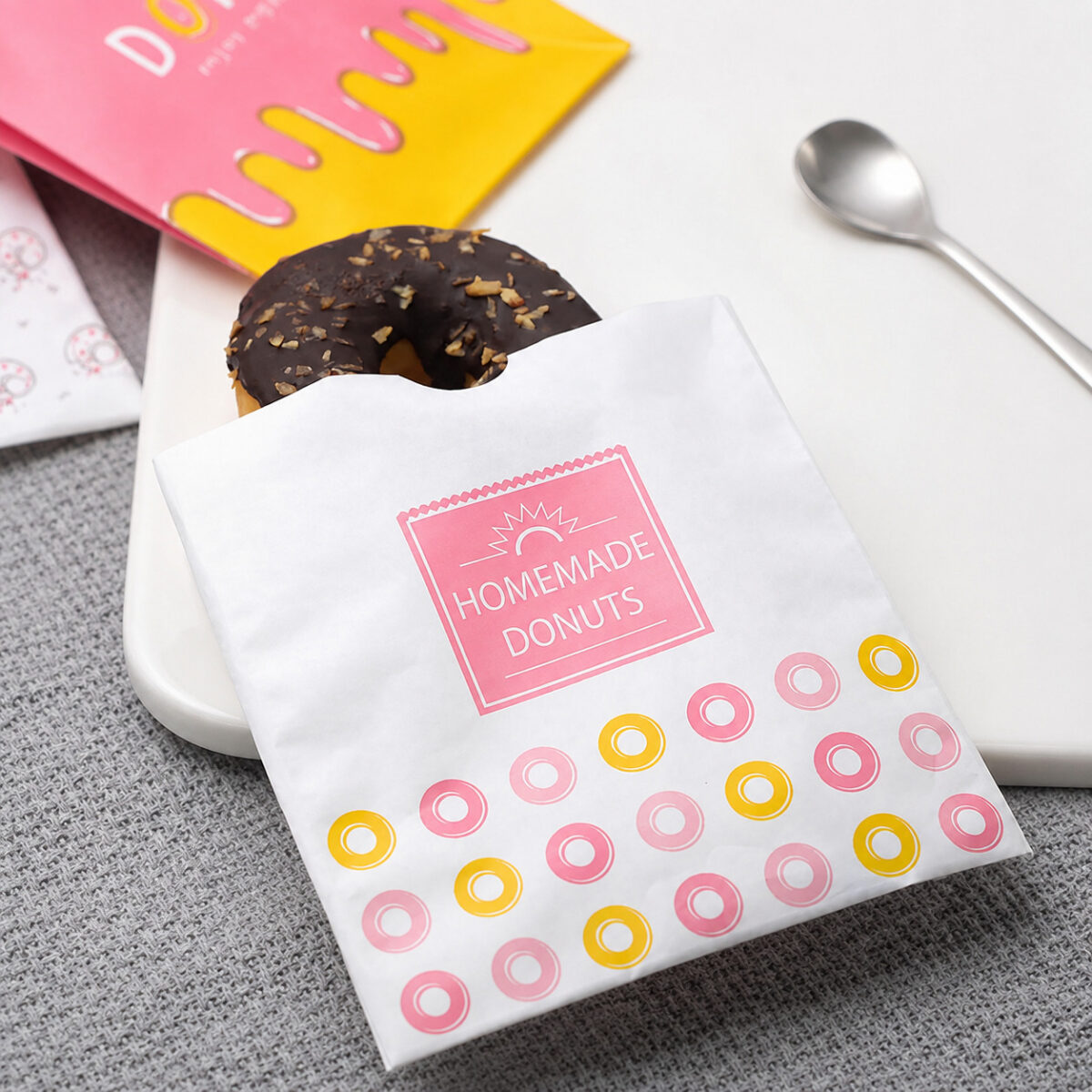 White Homemade Donuts sleeve with pink and yellow rings holding a chocolate donut on a white plate