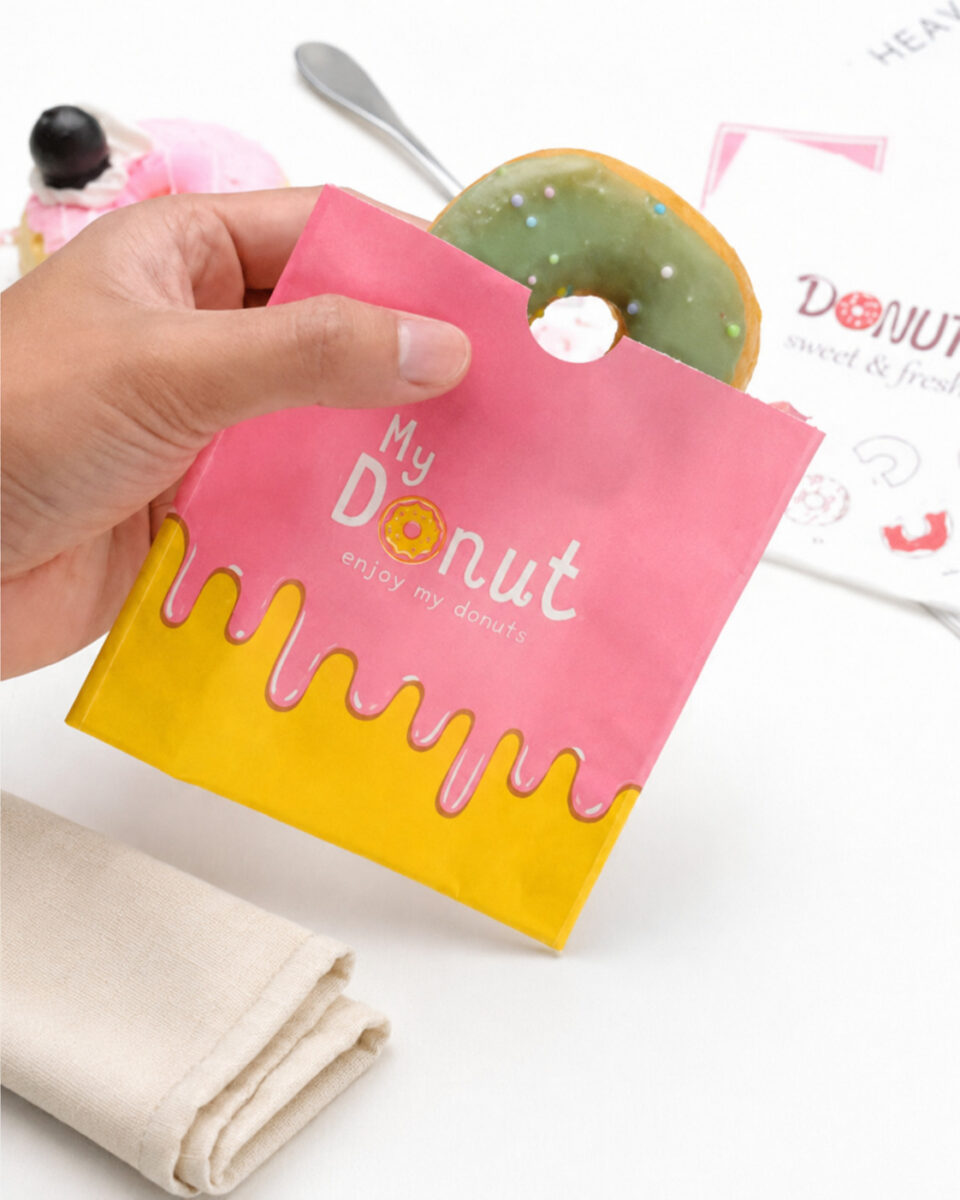 Pink My Donut paper sleeve with a green iced donut, held above a table beside folded linen