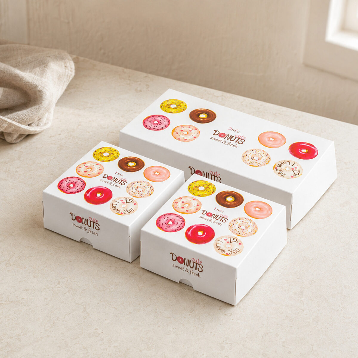 Printed Donut Assortment Boxes Two square and one rectangular white doughnut cartons with colorful doughnut artwork and front thumb notches
