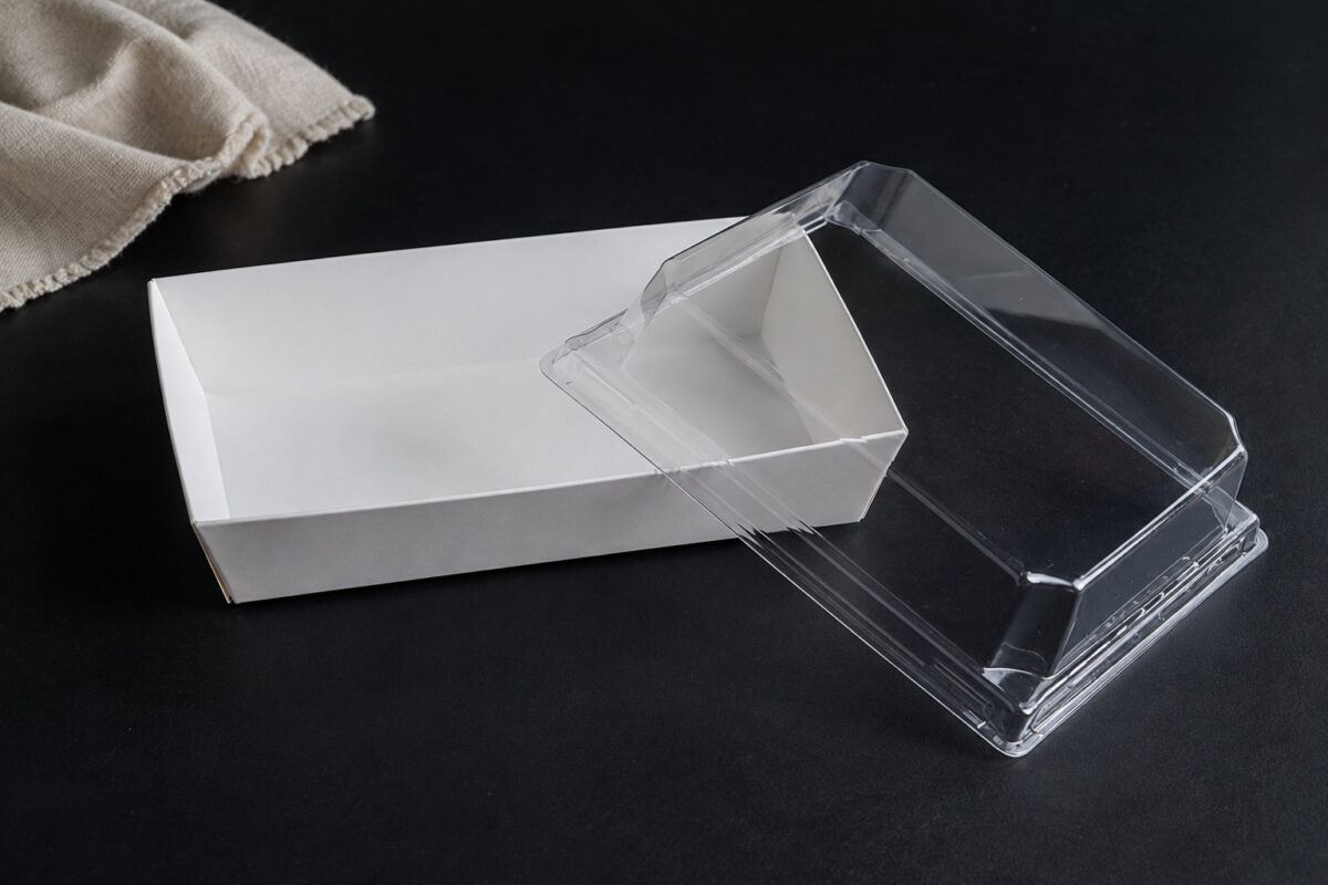 Empty white rectangular paper dessert tray beside its separate clear molded lid