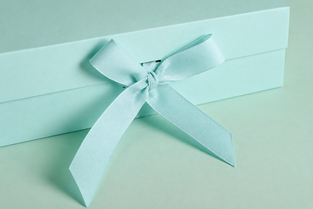 Mint green grosgrain ribbon bow threaded through a gift box closure slit