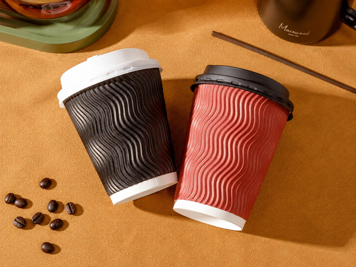 Two red and dark brown ripple wall coffee cups with black and white lids on mustard cafe linen