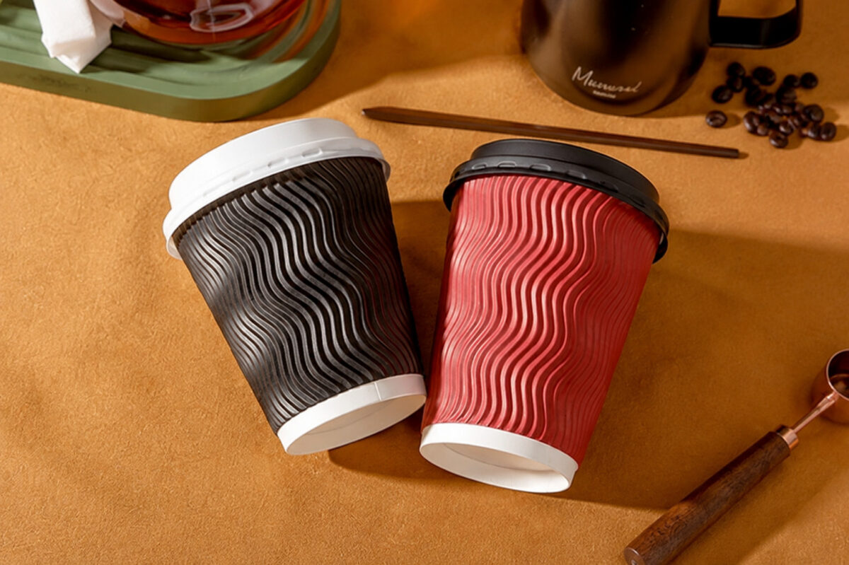 Red and dark ripple wall cups with fitted black and white lids beside cafe utensils