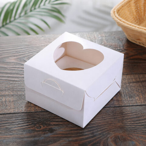 White dessert carton with a heart-shaped top window and folded front locking tab on a wood table