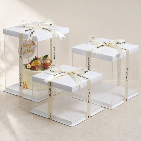 Three clear square cake boxes with white lids and ivory ribbons, shown in tall, medium and low heights