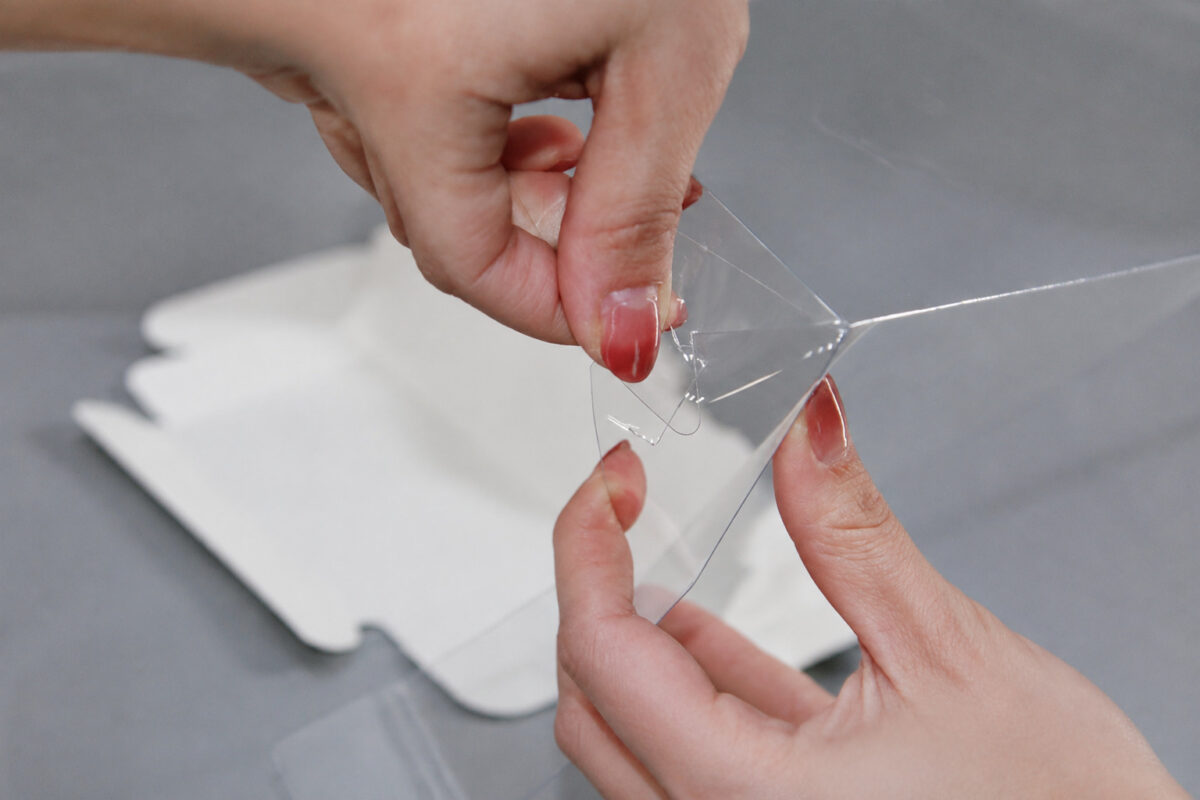 Hands joining the clear locking tab and slot on a transparent cake box wall