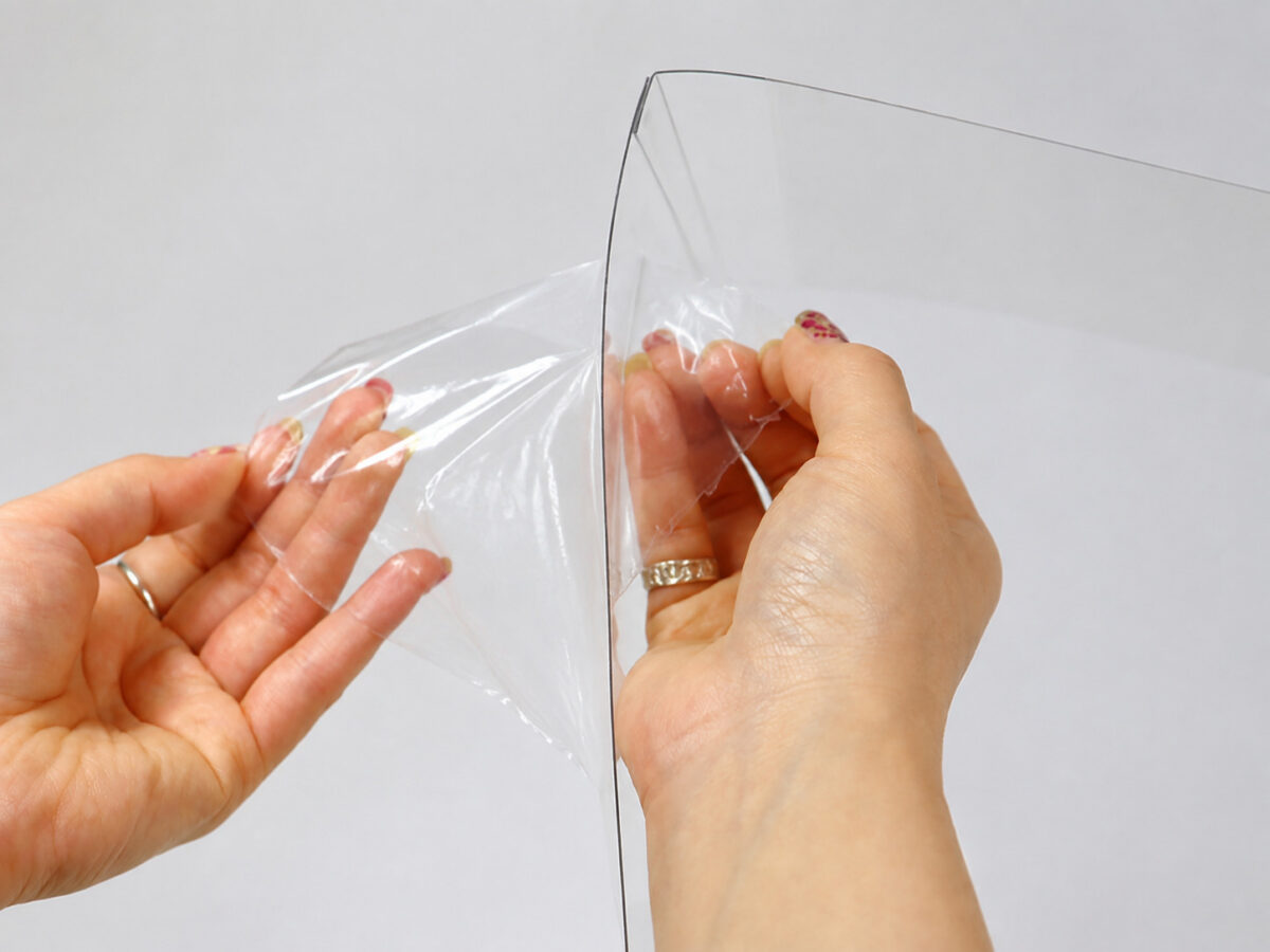 Hands peeling protective film from a clear cake box panel