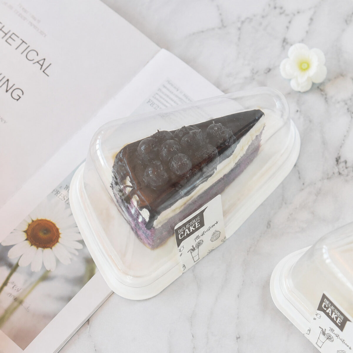 Clear triangular cake slice box with a white base and chocolate layer cake on a marble table