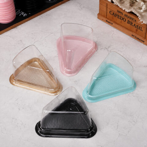 Four clear triangular cake slice containers with gold, pink, turquoise and black bases