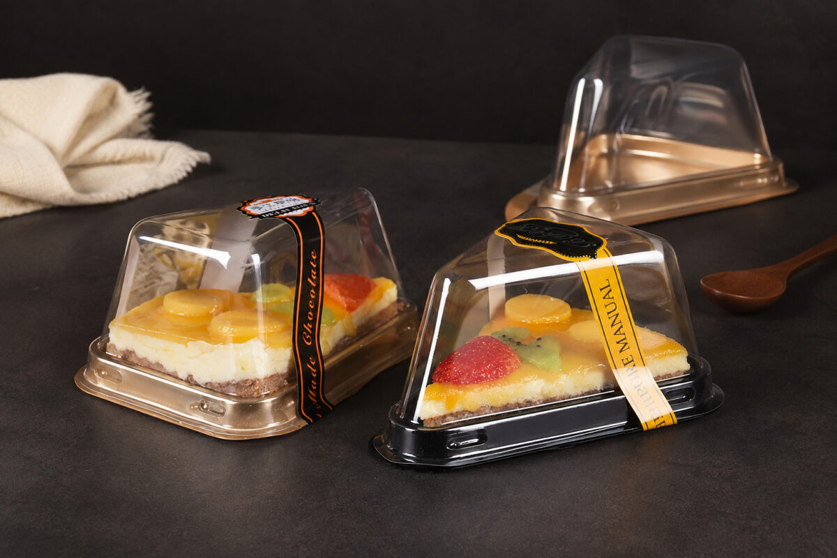 Fruit cake slices in gold and black triangular containers with clear lids