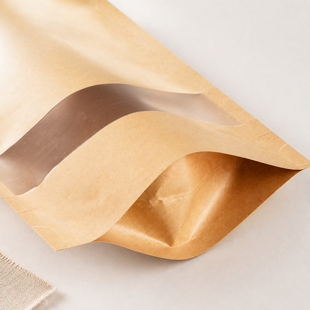 Close-up of the curved bottom gusset and transparent window film on a kraft stand-up pouch