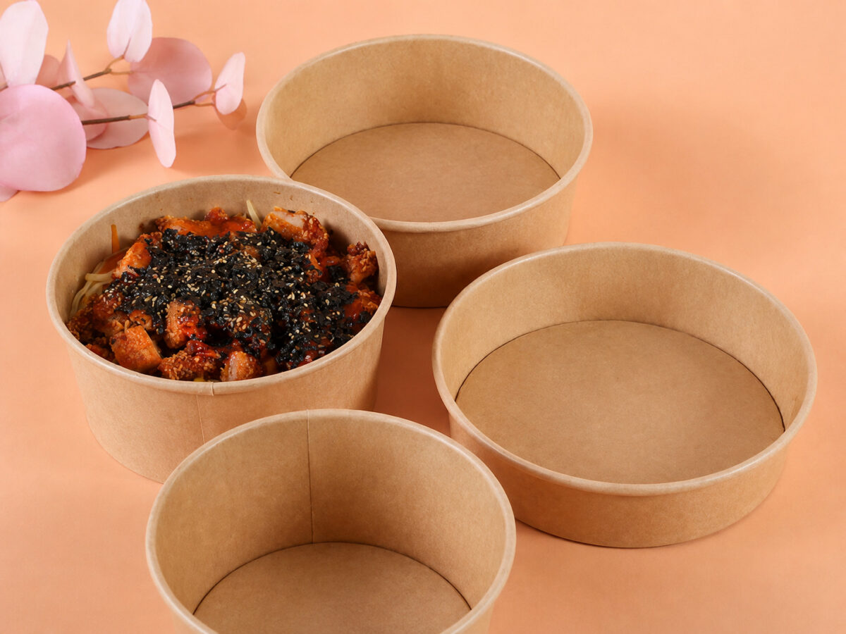 Four kraft food bowls in different sizes, including one prepared meal, on a peach tabletop